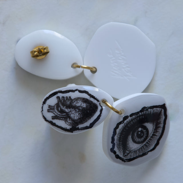 Gros plan sur les motifs cœur anatomique et œil des boucles d’oreilles DRAMARAMA en acrylique blanc