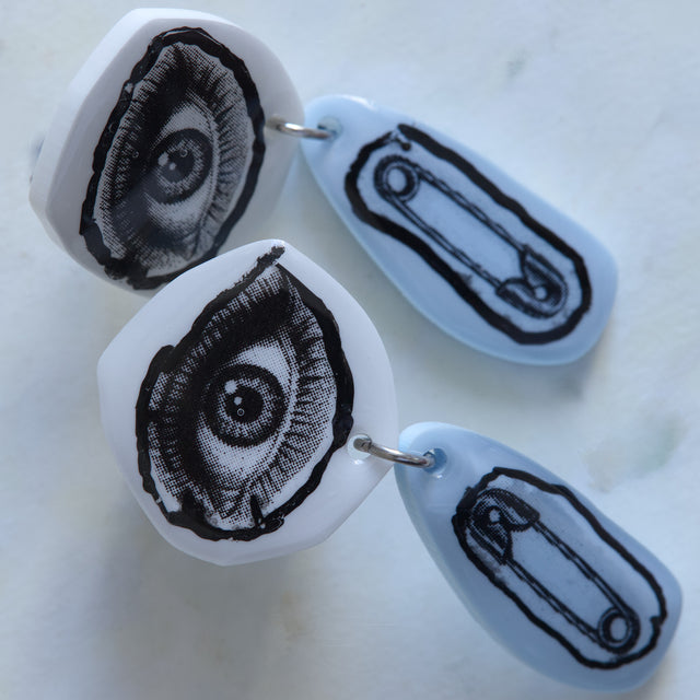 Gros plan sur les motifs œil et épingle à nourrice des boucles d’oreilles DRAMARAMA