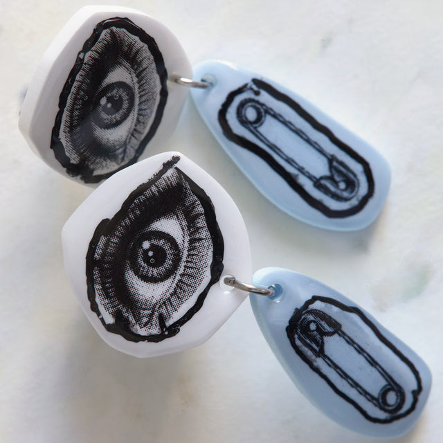 Gros plan sur les motifs œil et épingle à nourrice des boucles d’oreilles DRAMARAMA
