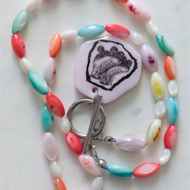 Gros plan sur le pendentif patins à roulettes et les perles de nacre multicolores du collier DRAMARAMA
