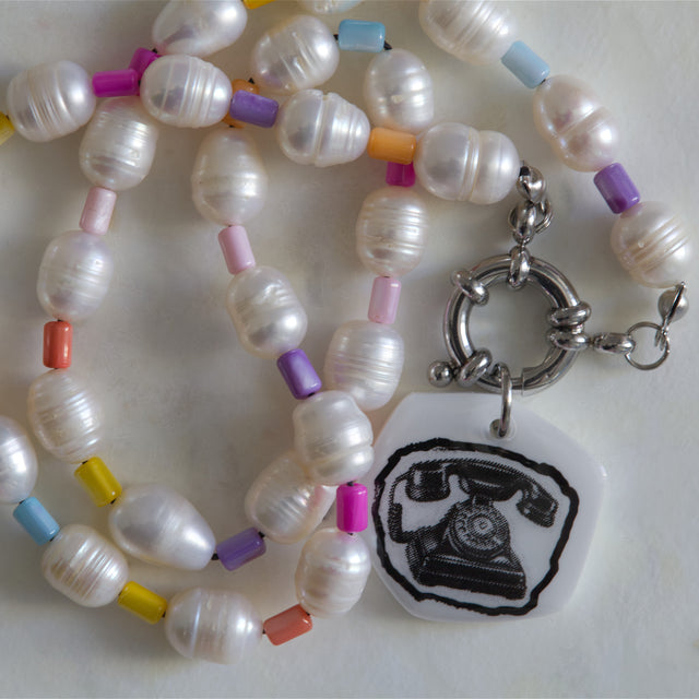 Gros plan sur le pendentif téléphone en acrylique et les perles d’eau douce du collier DRAMARAMA