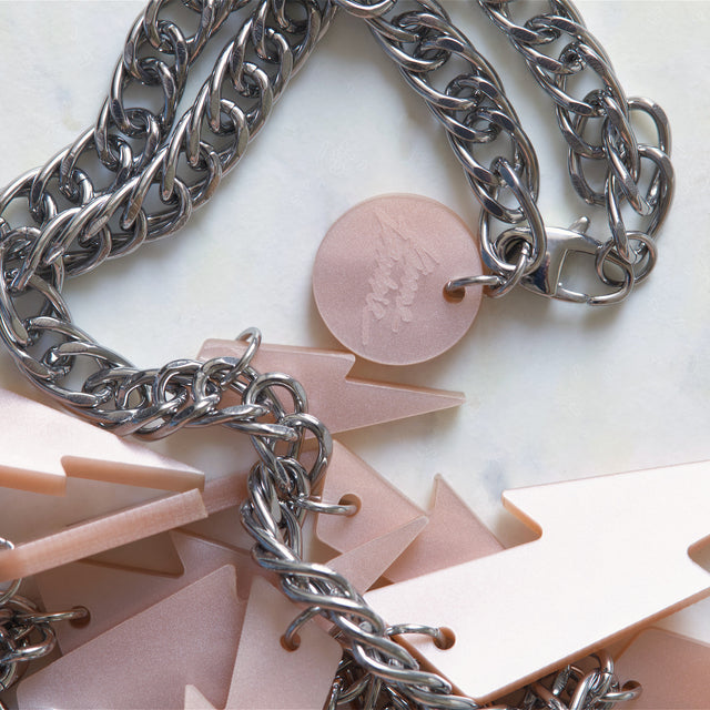 Détail du collier plastron Electric Feel avec éclairs en acrylique rose nacré et chaîne argentée