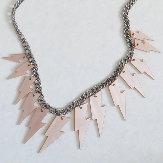 Détail du collier plastron Electric Feel avec éclairs en acrylique rose nacré et chaîne argentée