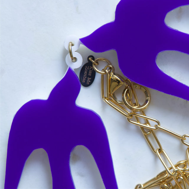 Gros plan sur les hirondelles violettes, la chaîne dorée et le fermoir du collier Henri