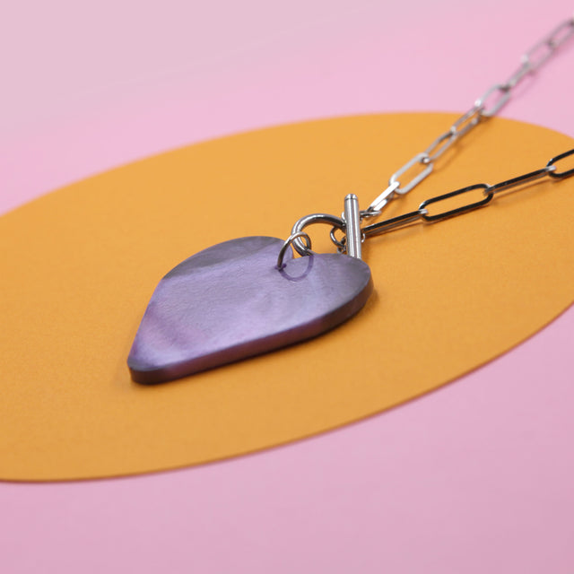 zoom sur le pendentif collier cœur violet – accessoire mode pour un look audacieux et tendance sur un fond coloré.