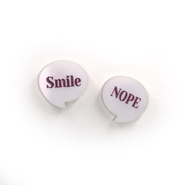 close up of smile & nope laser cut pearly white acrylic pin brooches. one say smile, the other one nope. on a white background.