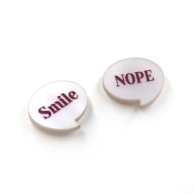 side view of smile & nope laser cut pearly white acrylic pin brooches. one say smile, the other one nope. on a white background. 