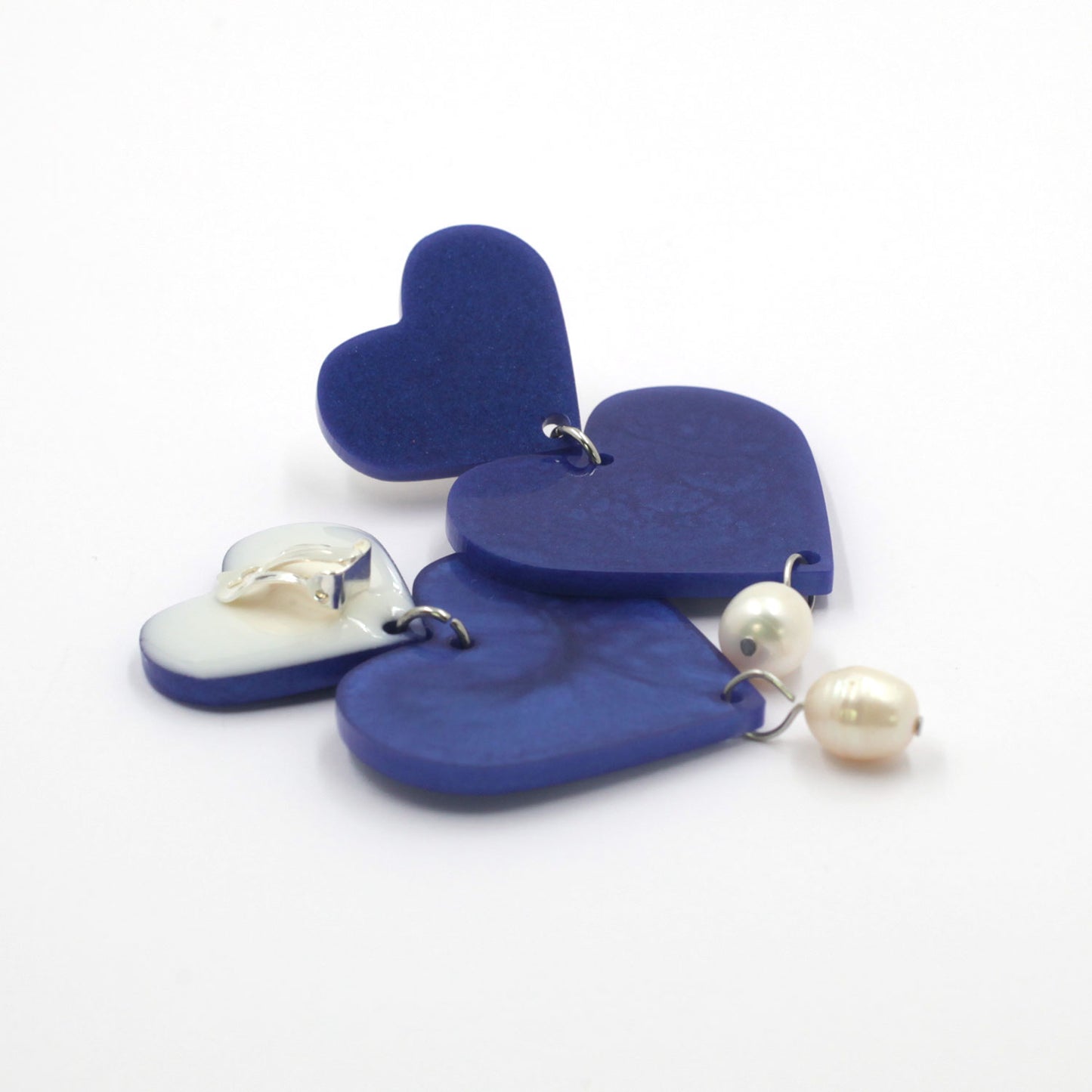 This is a picture of blue hearts earrings with freshwater pearls on a white background.  one is on the back, the clip on are silver with silicone pad protection. 