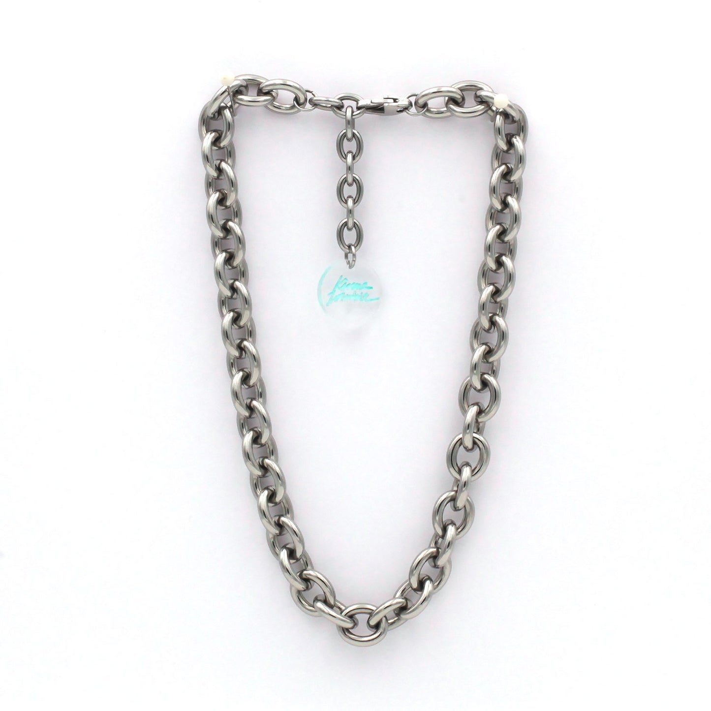 this is a picture of a massive link cable chain choker necklace hanging from a white background. there is an extender with a clear engraved medal with green signature logo. 