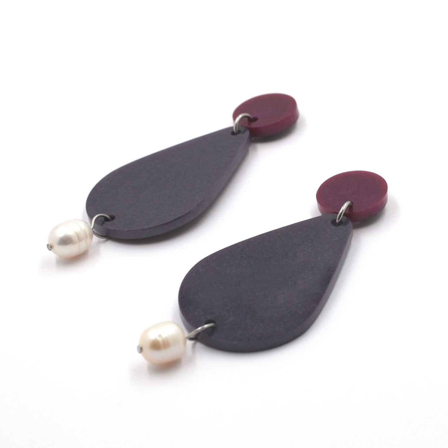 picture of earrings on a white background. the earrings are composed by a pink dot at the top, then a bigger purple pear shape and a freshwater pearls at the bottom hanging.