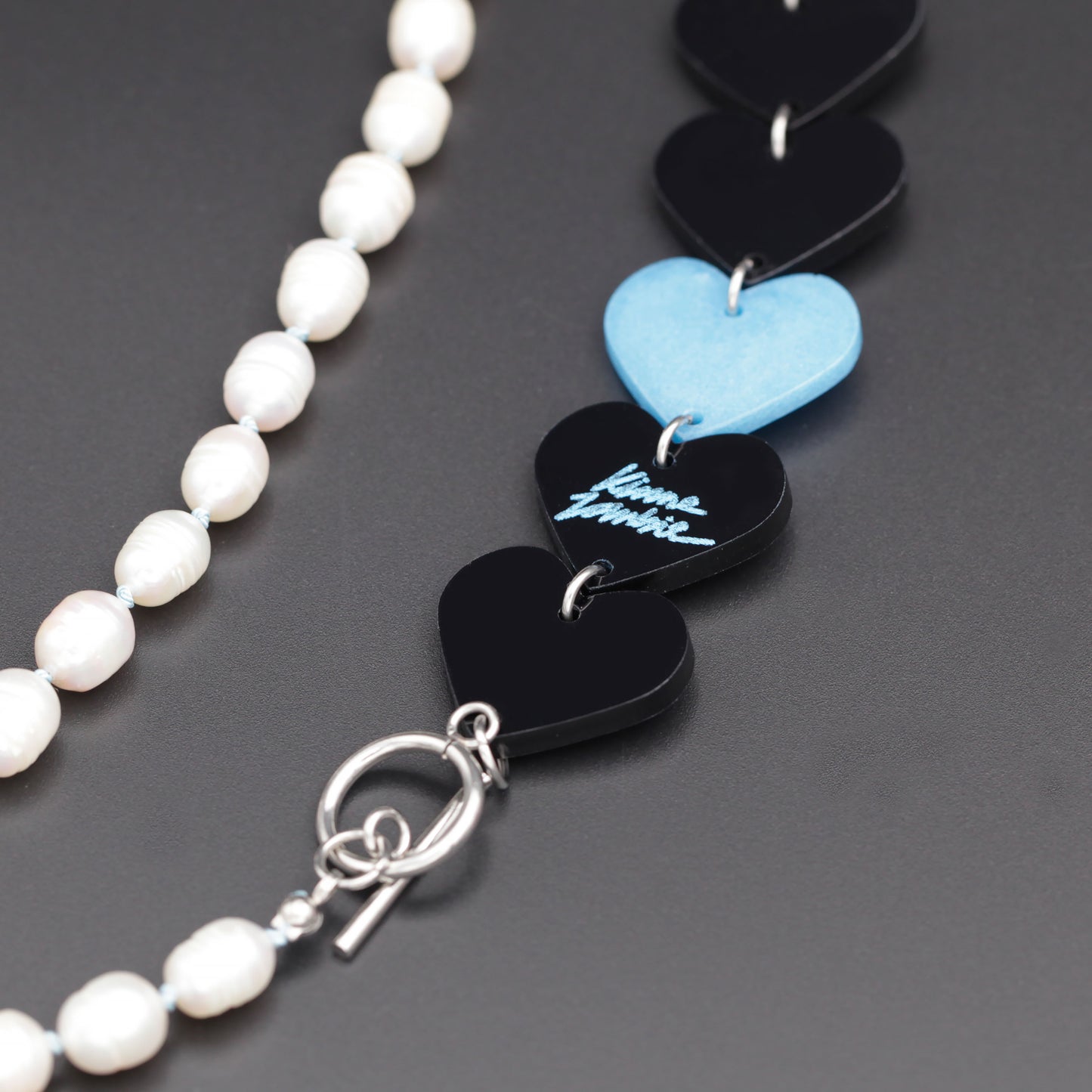 Close-up of a laser-cut and resin black and blue hearts necklace with freshwater pearls on a black background. 
