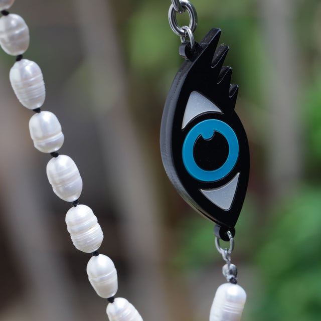 Close-up of a laser-cut evil eye and freshwater pearls necklace on a vegetal background. 
