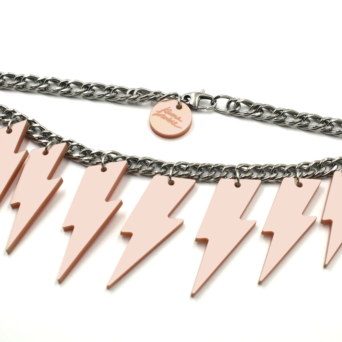 This is close up photo of a necklace composed of a chunky silver tone curb chain pink pearly lightning bolts of graduant size on a white background. on the lobster clasp there is a round charm with the kissmezombie logo engraved on it. 