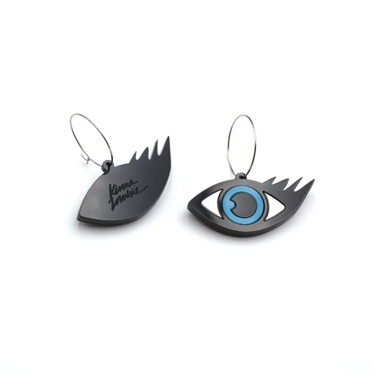 on a white background, a pair of black, white and blue laser cut evil eye hoops earrings, one of the earring is on its back, there is an engraved logo kiss me zombie