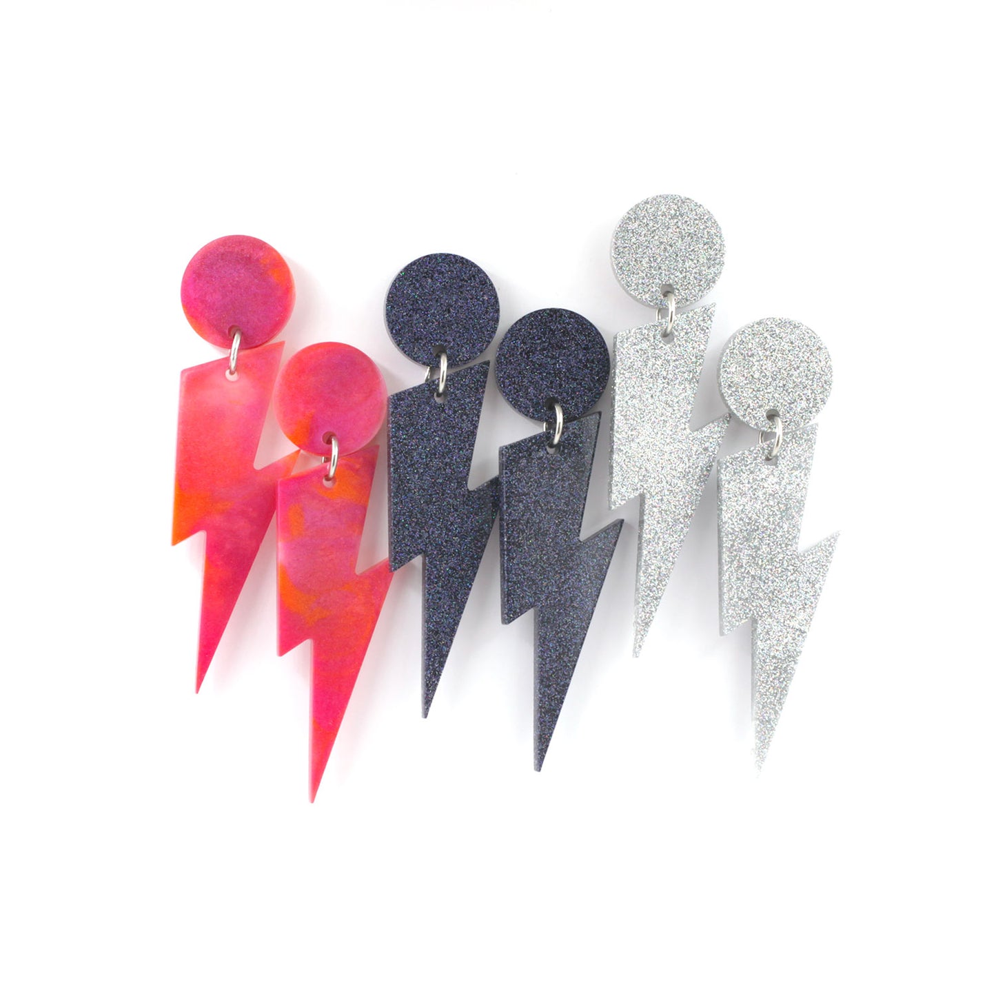 this is a picture of three pairs of bolts dangle earrings on a white background. On the left, the earrings are pink, orange marbled, at the center, the earrings are black holographic glitter and at the right side, silver holographic glitter.