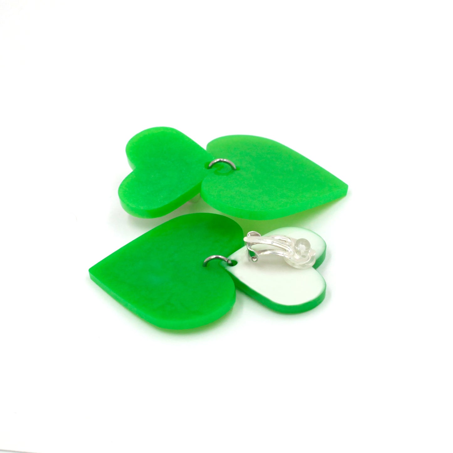 lime green hearts earrings on a white background. one is on its back, there is a clip on earring with a silicone pad protection. the top of the earring is white, the pendant heart is the same lime green from the front.