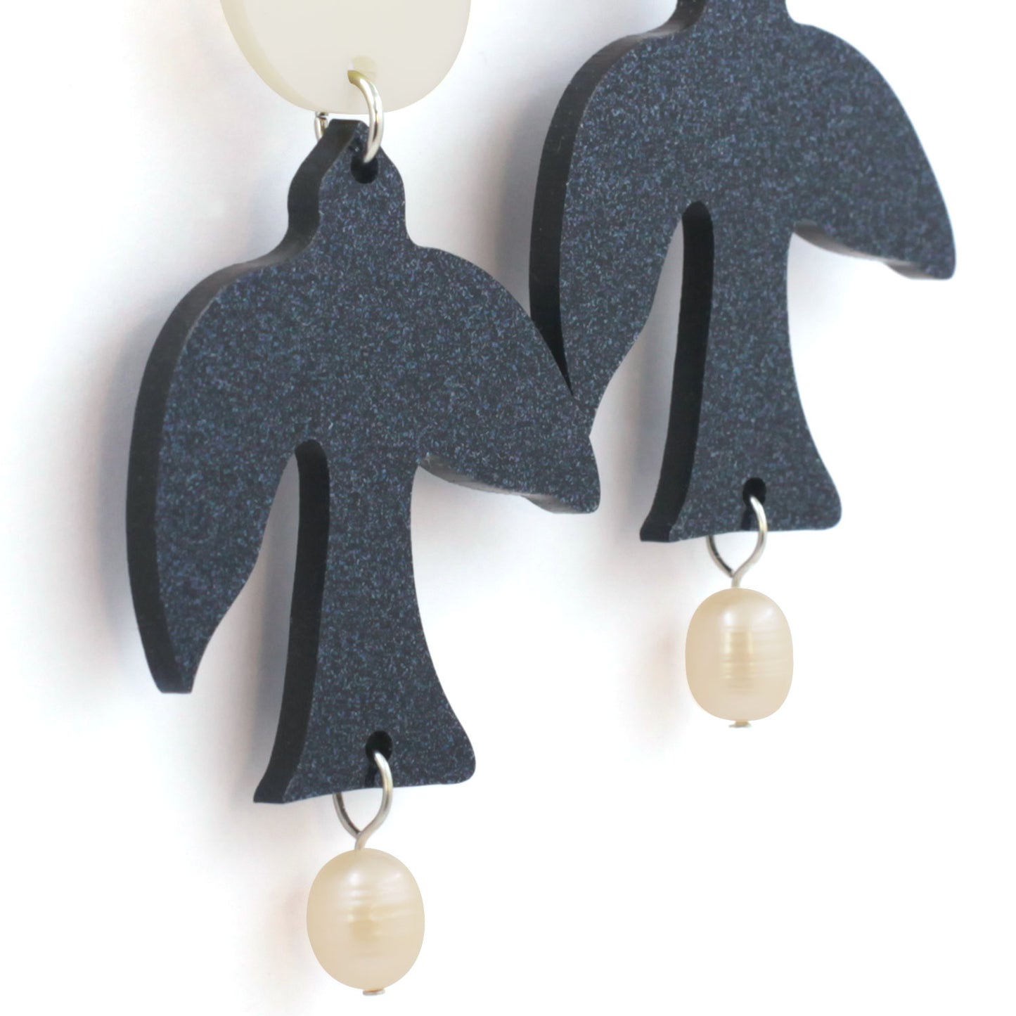 This is a close up of a pair of earrings. there are glitter dark blue birds with two freshwater pearls hanging from the tail and a white round piece on top. the background is white.