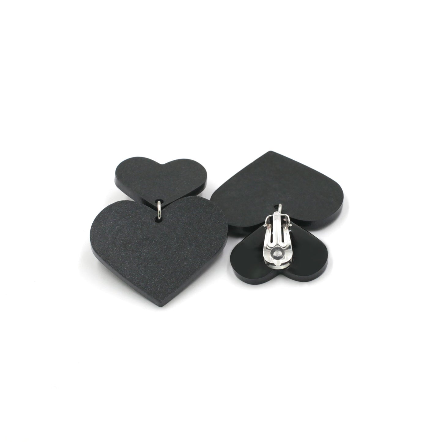 black hearts earrings on a white background. one is on its back, there is a clip on earring with a silicone pad protection. 