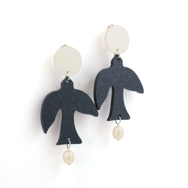 This is a pair earrings. there are glitter dark blue birds with two freshwater pearls hanging from the tail and a white round piece on top. the background is white.