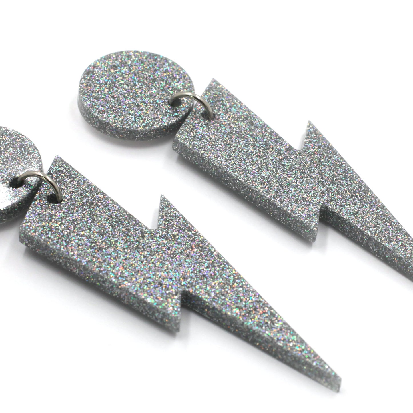 this is a close up picture of silver holographic glitter bolt and dot dangle earrings on a white background. 