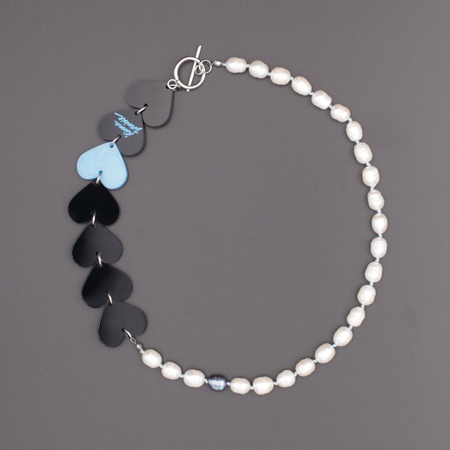 Laser-cut and resin black and blue hearts necklace with freshwater pearls and toggle clasp on a black background. 